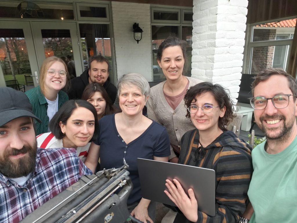 Arbeitsgruppe Digitale Forensische Linguistik auf einem Schreib-Retreat. 9 Menschen schauen lächelnd in die Kamera, zwei halten eine Schreibmaschine bzw. ein Laptop.